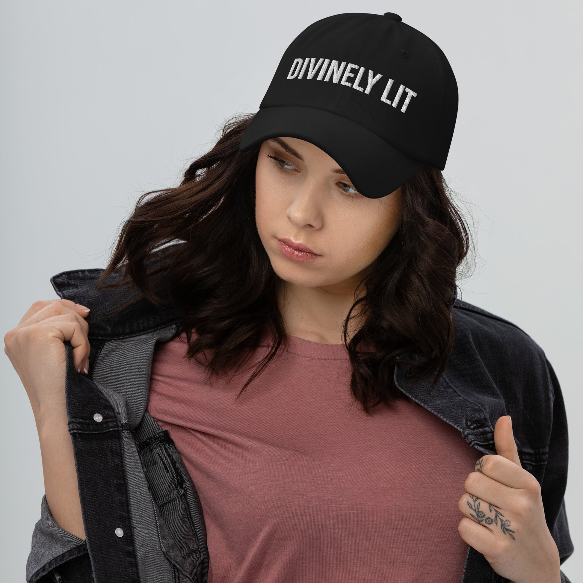 Woman wearing a black cap with 'DIVINELY LIT' text on a plain background