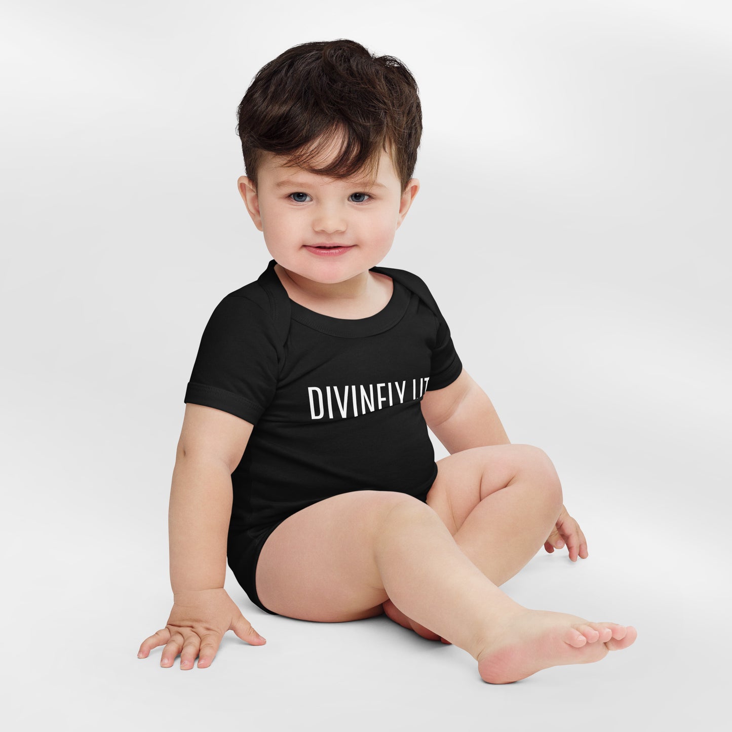 Baby wearing a black onesie with 'DIVINELY LIT' text on a white background