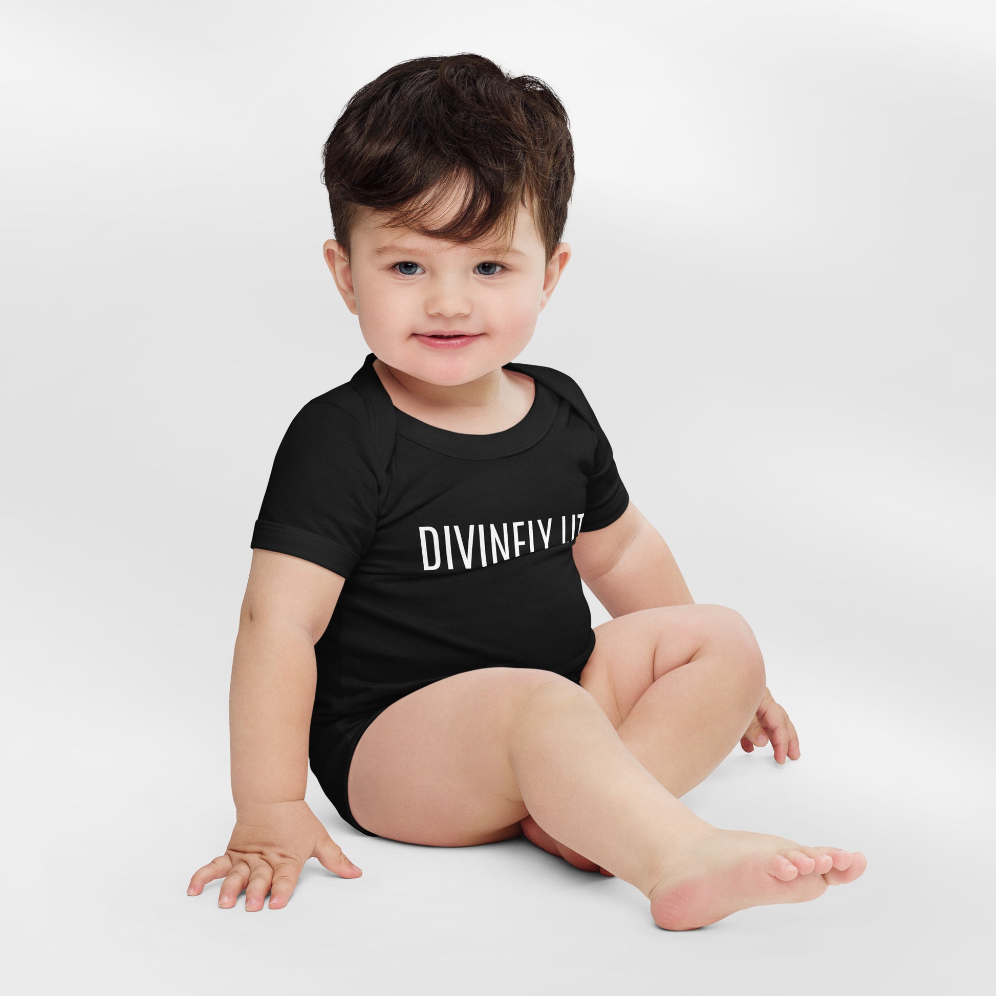 Baby wearing a black onesie with 'DIVINELY LIT' text on a white background