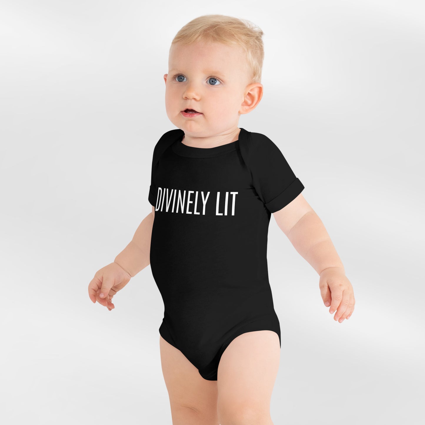 Baby wearing a black onesie with 'DIVINELY LIT' text on a white background
